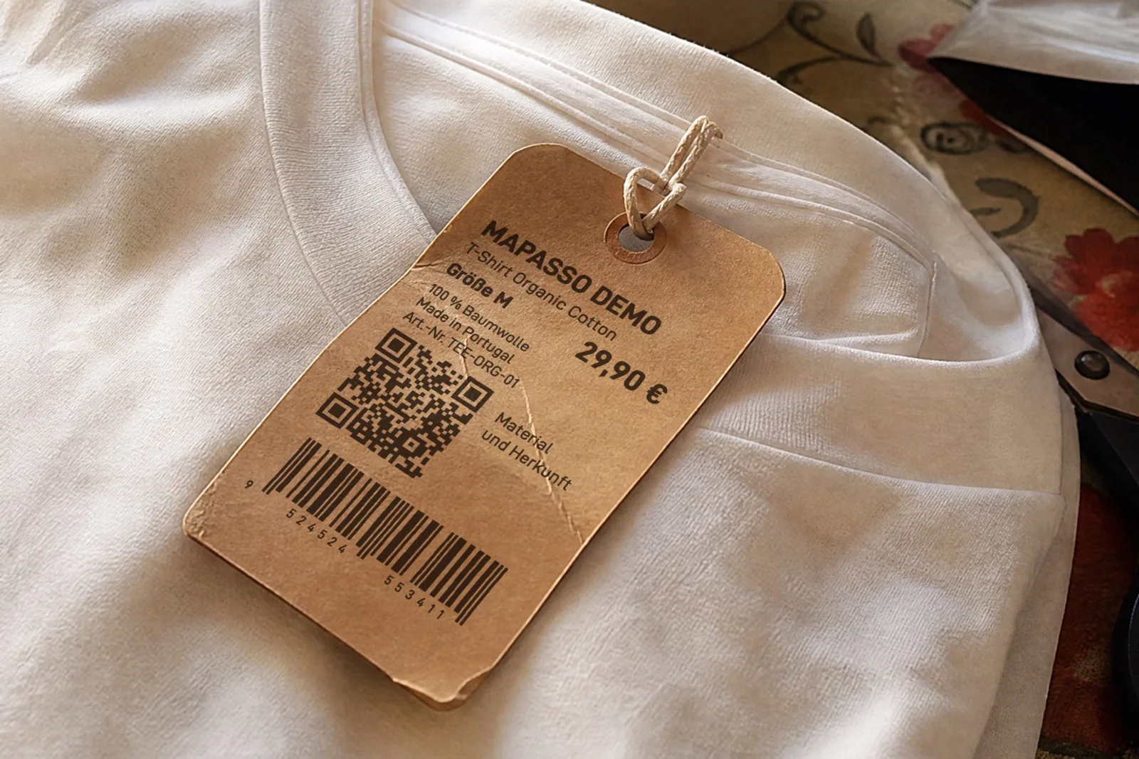 KI-generiertes Bild: Hangtag aus Kraftpapier an einem T-Shirt mit „Mapasso Demo“, „T-Shirt Organic Cotton“, Größe M, 29,90 €, „100 % Baumwolle“, „Made in Portugal“, QR-Code mit dem Text „Material und Herkunft“ und Strichcode